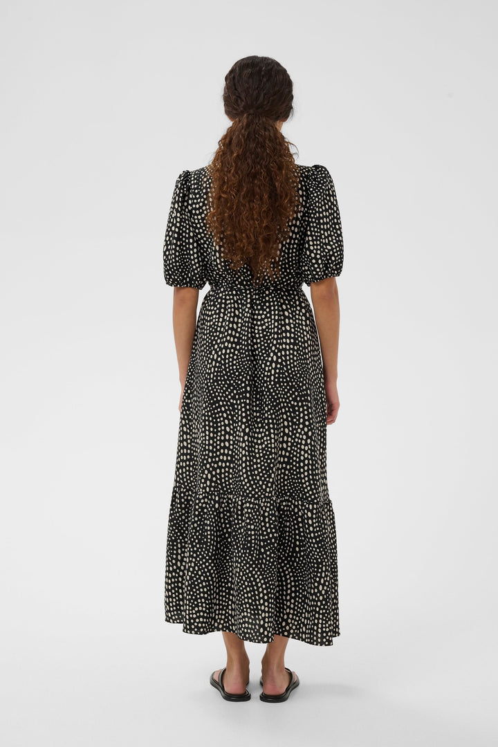 Femme portant une robe longue imprimée à taille ceinturée avec encolure en V et manches courtes bouffantes.