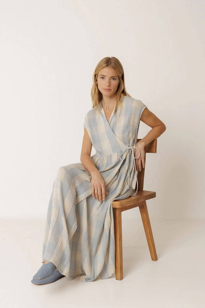 Femme portant une robe longue portefeuille à carreaux en position assise sur une chaise en bois