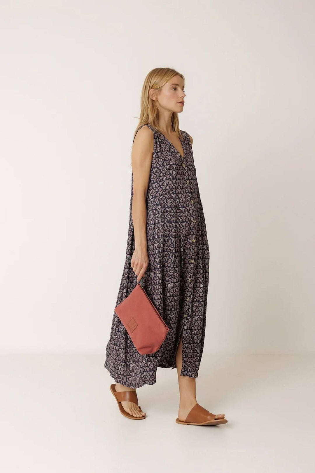 Femme portant une robe longue réversible à imprimé, tenue fluide et sans manches, avec un sac rose, confort d'été polyvalent.
