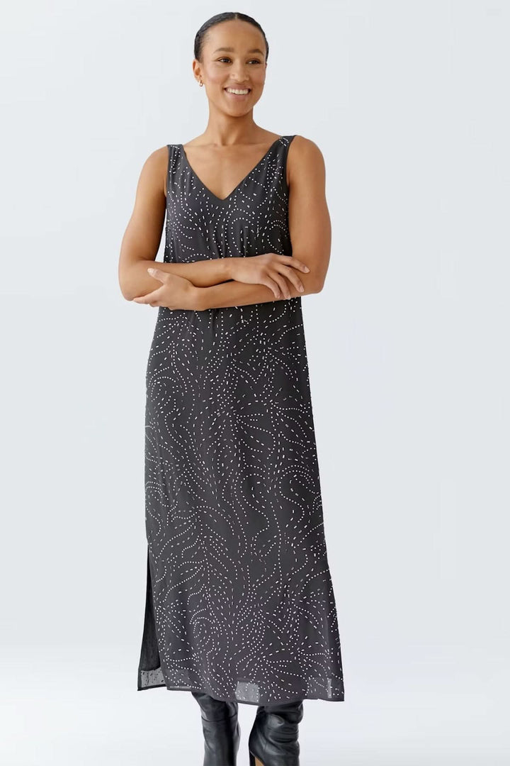 Femme portant une robe longue sans manches avec imprimé discret et encolure en V, accompagnée de bottes noires, look chic et contemporain.