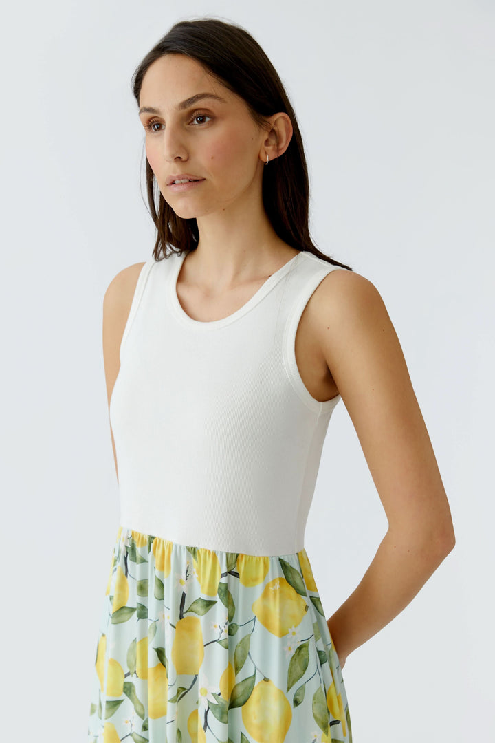 Femme portant une robe longue sans manches à jupe fluide avec motif citron et haut blanc.