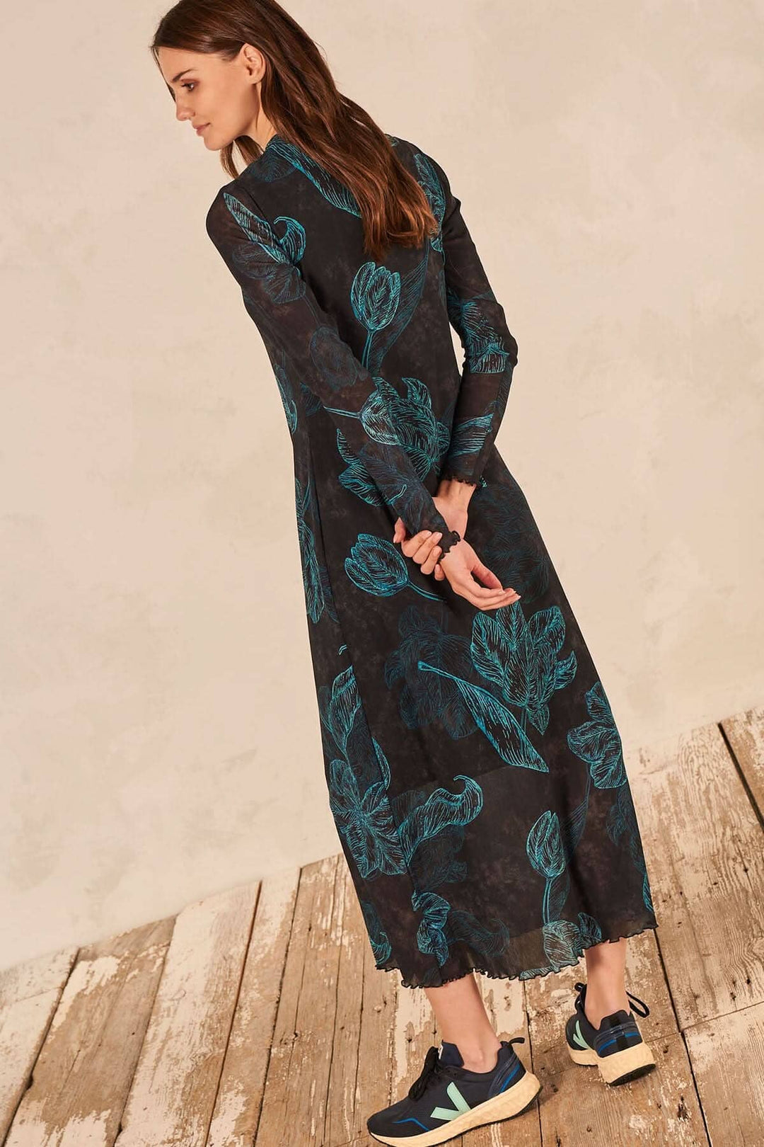 Robe longue à manches transparentes avec imprimé feuilles, portée avec des baskets sur un sol en bois.