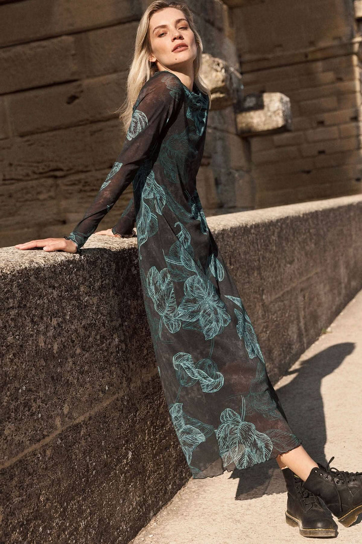 Jolie robe longue à manches transparentes avec un imprimé de feuilles, portée avec des bottes pour un look décontracté.