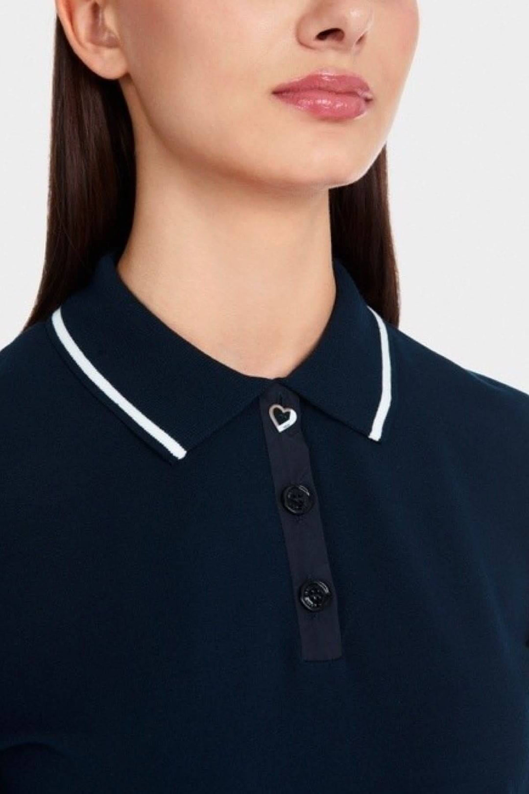 Détails d'un polo femme avec col contrasté, boutons noirs et motif en cœur sur le col.