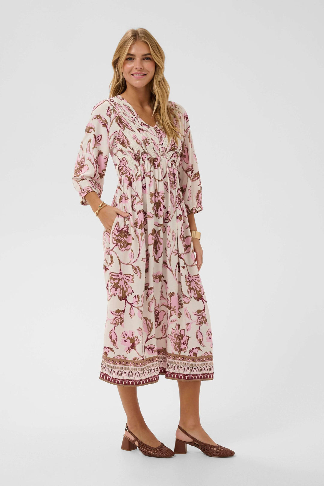 Femme portant une robe midi fluide à imprimé floral avec manches trois-quarts, encolure en V, et taille froncée.