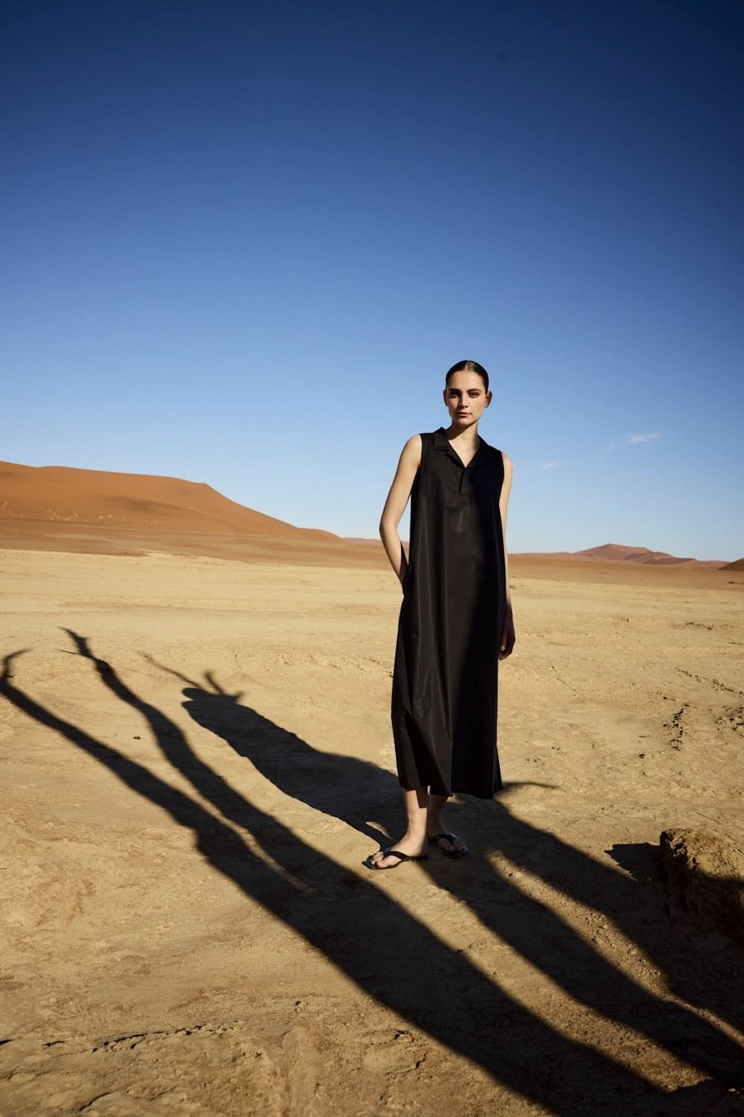 Femme portant une robe midi sans manches à col chemise dans un paysage désertique, alliant élégance et modernité.