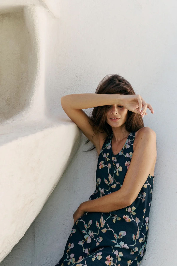 Femme portant une robe midi sans manches à imprimé floral, posant contre un mur blanc, mettant en valeur le style fluide et élégant de la robe.