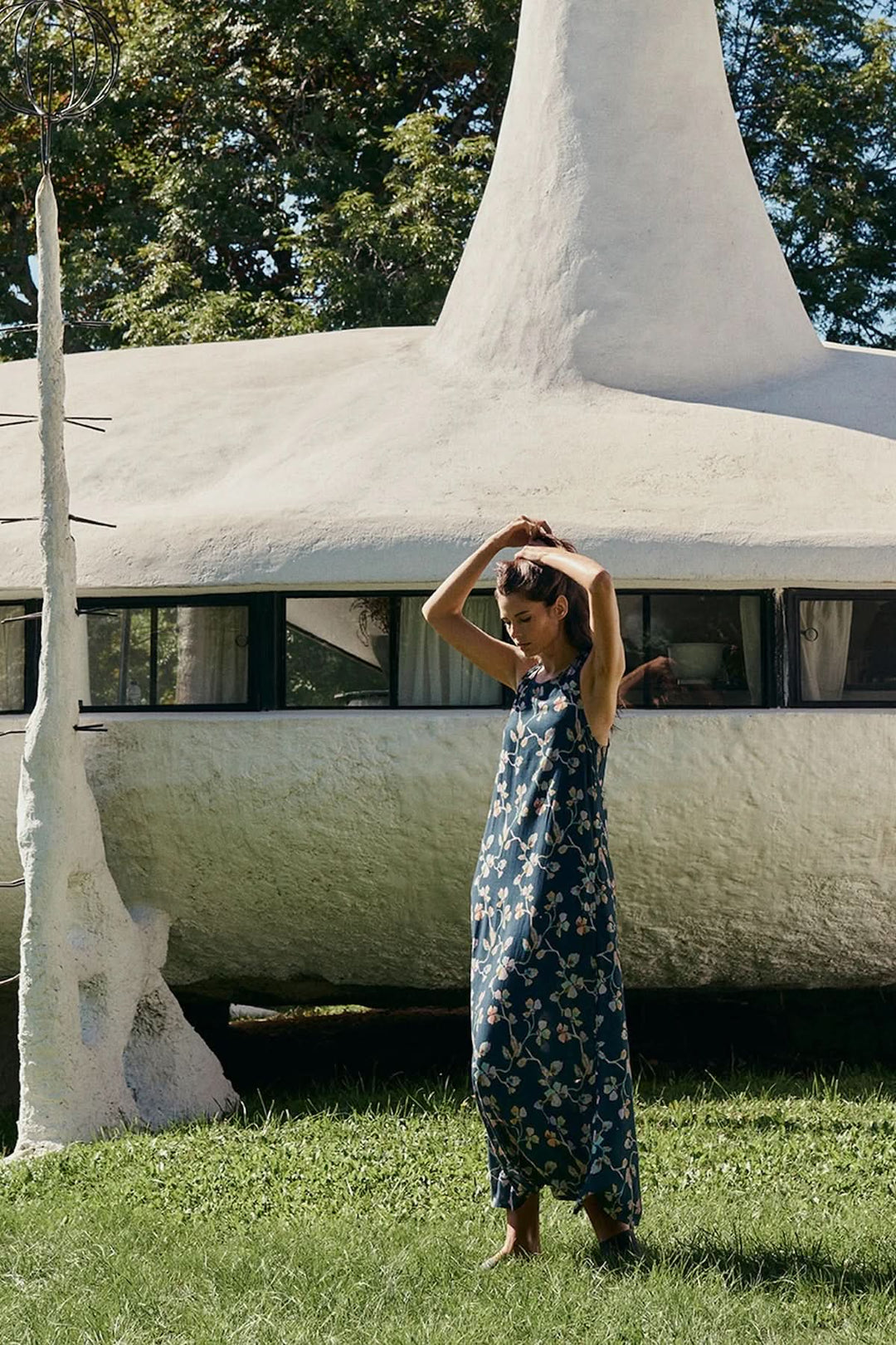 Femme portant une robe midi sans manches à imprimé floral devant une structure moderne.