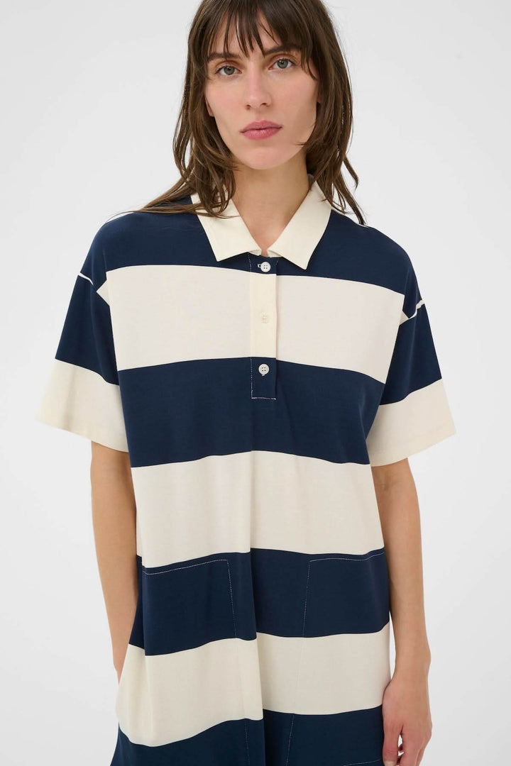 Femme portant une robe polo Alise à rayures larges, coupe droite, col polo, allure sport chic moderne et structurée.