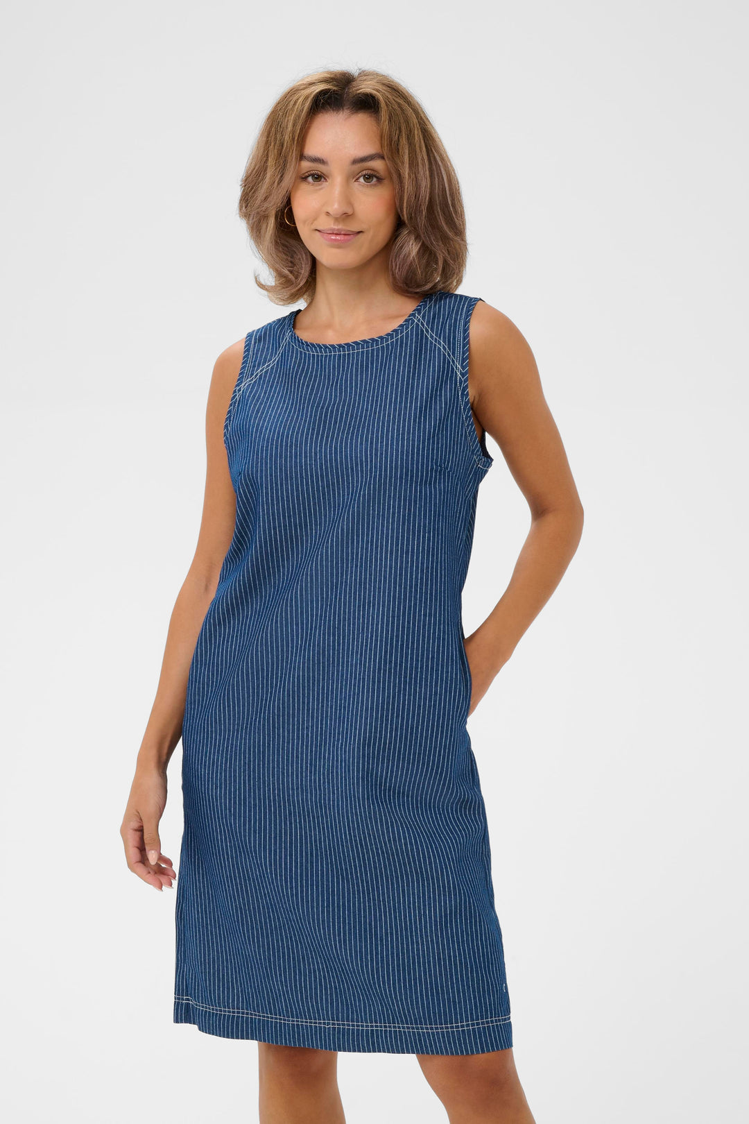 Femme portant une robe sans manches Agate à fines rayures bleues avec surpiqûres, silhouette épurée et décontractée.
