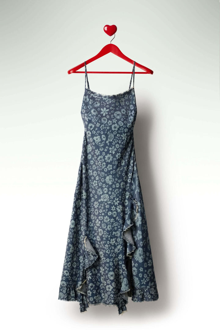 Robe à volants en denim à motifs floraux, fines bretelles et volants asymétriques, sur un cintre rouge en forme de cœur.