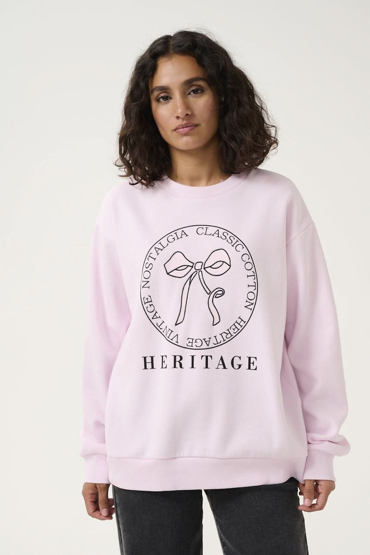 Woman wearing a pink Sweat-Shirt Ellen featuring a central bow graphic, perfect for a casual yet stylish look.