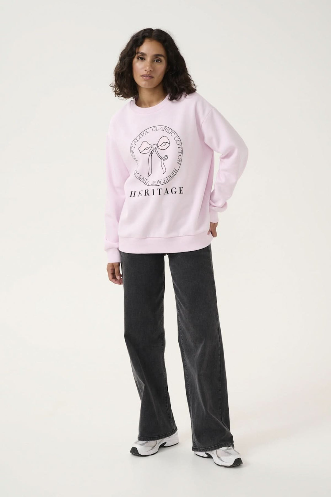 Casual pink sweatshirt with a central bow motif and the word 'HERITAGE', paired with black wide-leg pants and sneakers.