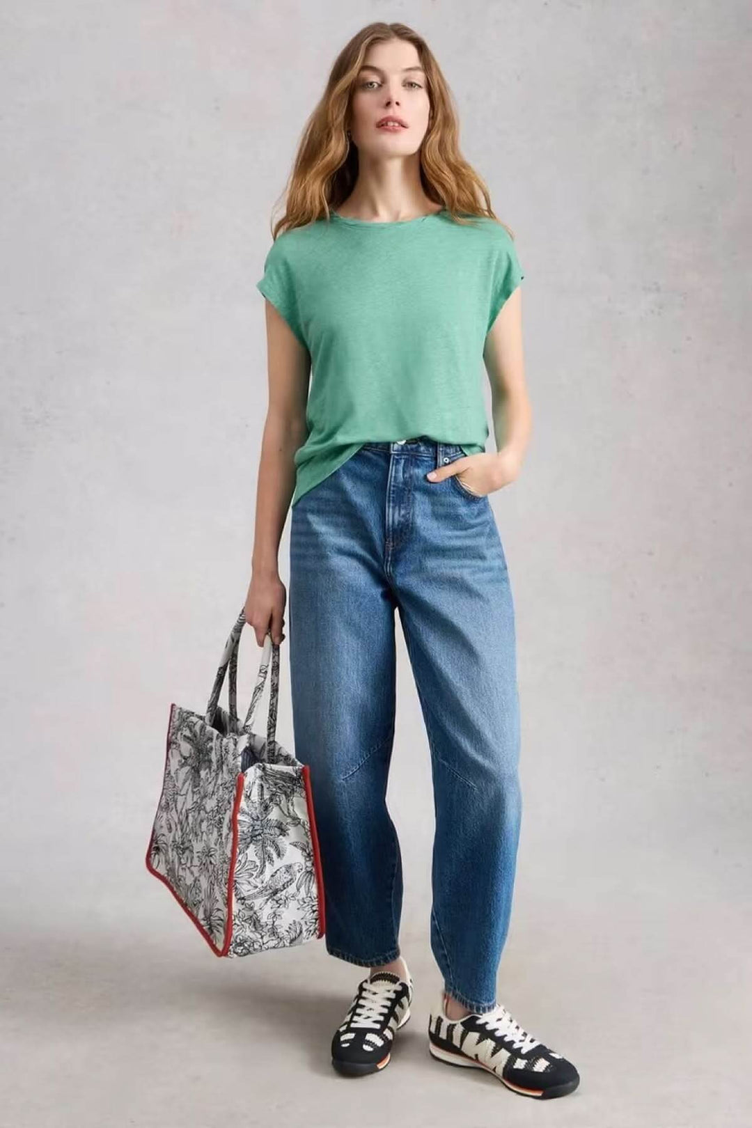 Femme portant un T-Shirt en lin Rowan vert, coupe ample, avec un jean et des baskets, tout en tenant un sac à main graphique.