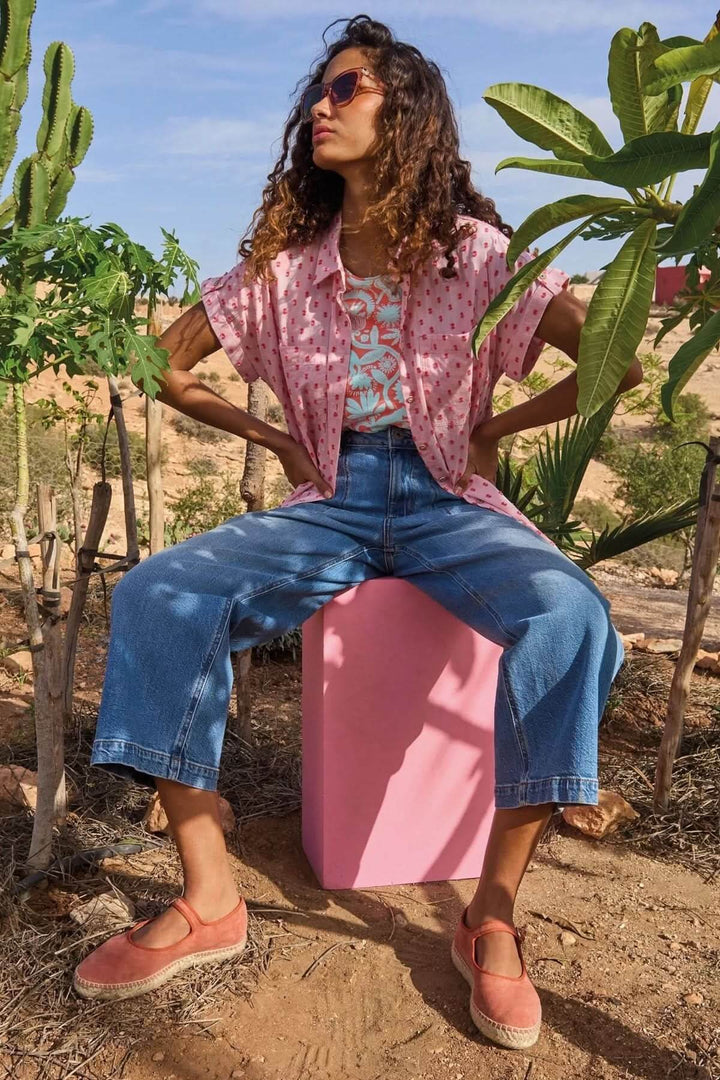 Femme assise sur un cube rose en tenue décontractée, t-shirt imprimé, jeans larges, cadre en plein air.