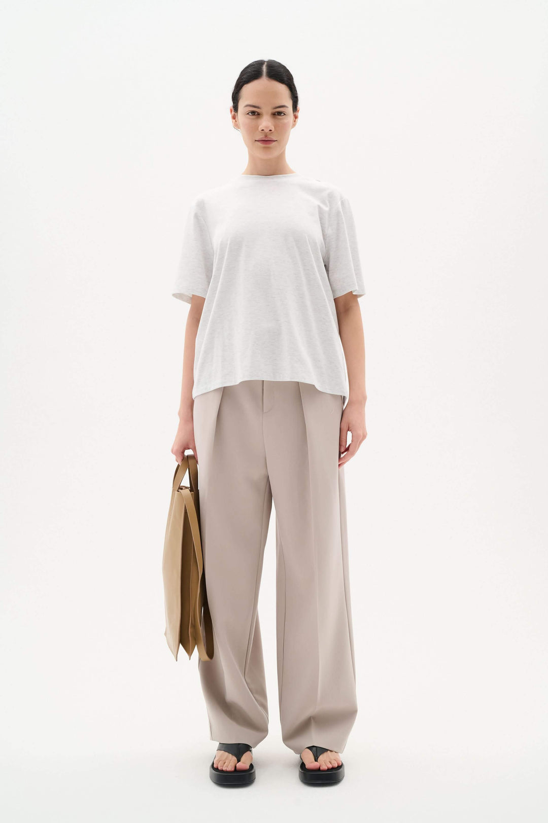 Model wearing the Amilla T-shirt with wide beige trousers and holding a brown bag, showcasing casual style.