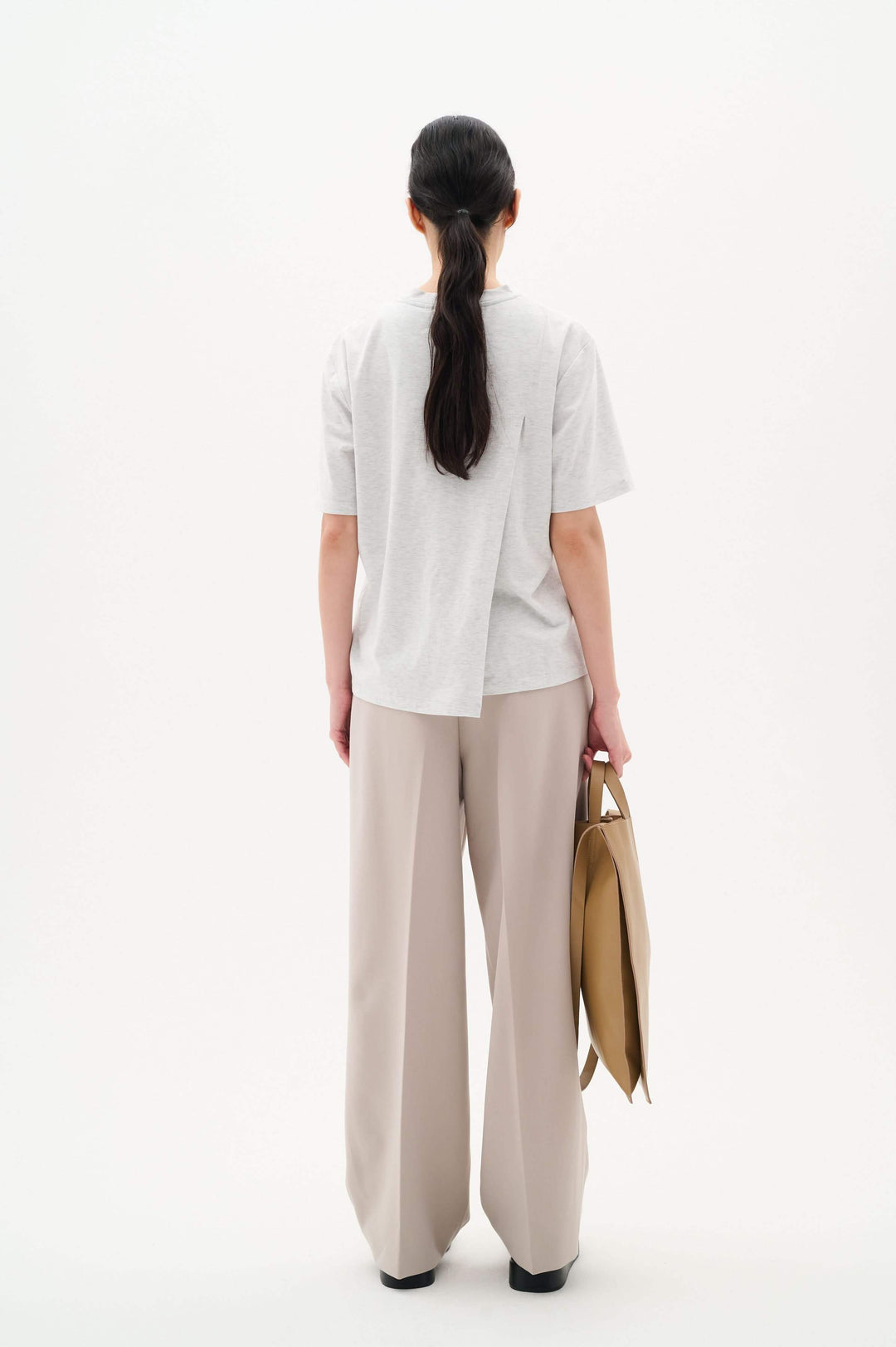 Back view of a woman wearing a relaxed-fit gray T-shirt Amilla and beige wide-leg trousers, holding a tan handbag.