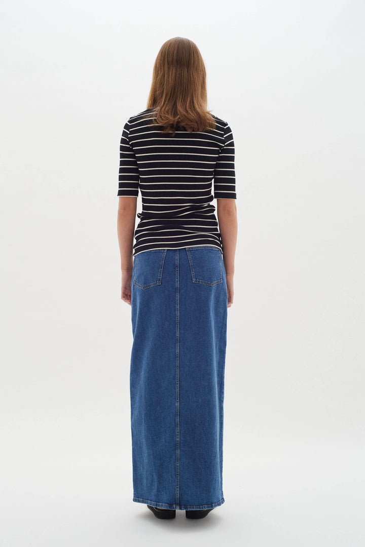 Femme vue de dos portant un t-shirt à rayures noires et blanches avec une jupe longue en jean.