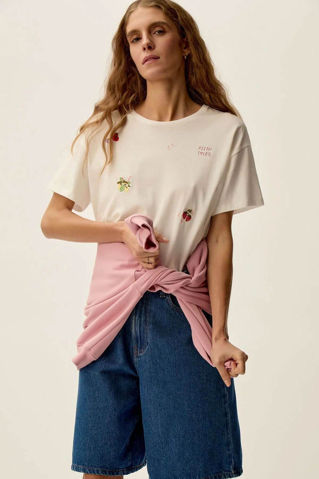 Femme portant un t-shirt Gamos avec motifs floraux, jeans en denim et un gilet rose noué autour de la taille.