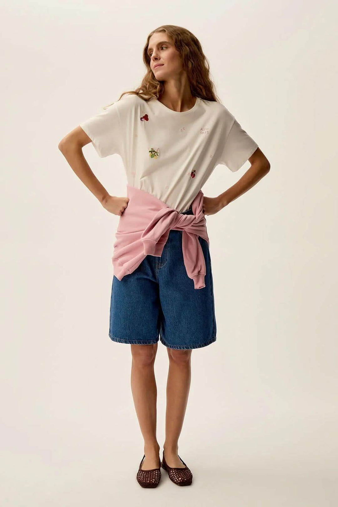Femme portant un t-shirt Gamos à motifs floraux, avec un short en jean et un pull noué à la taille.
