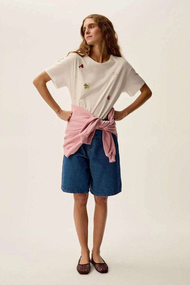 Femme portant un t-shirt Gamos à motifs floraux, avec un short en jean et un pull noué à la taille.