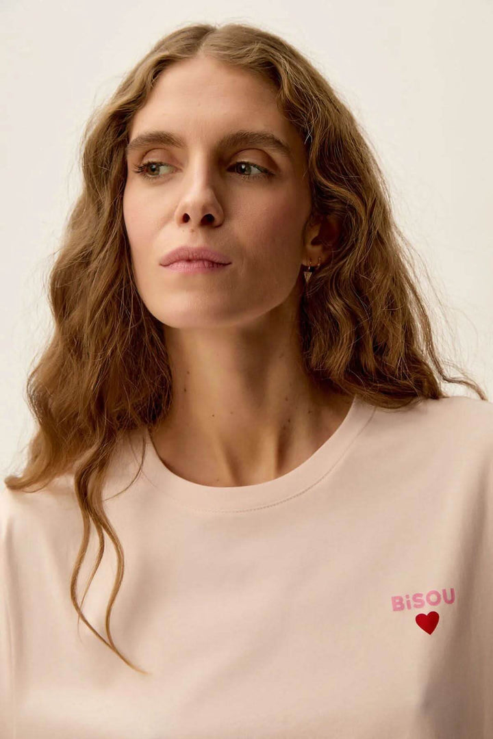 Femme portant un t-shirt rose nude Gazoline avec imprimé "Bisou" et coeur sur la poitrine.