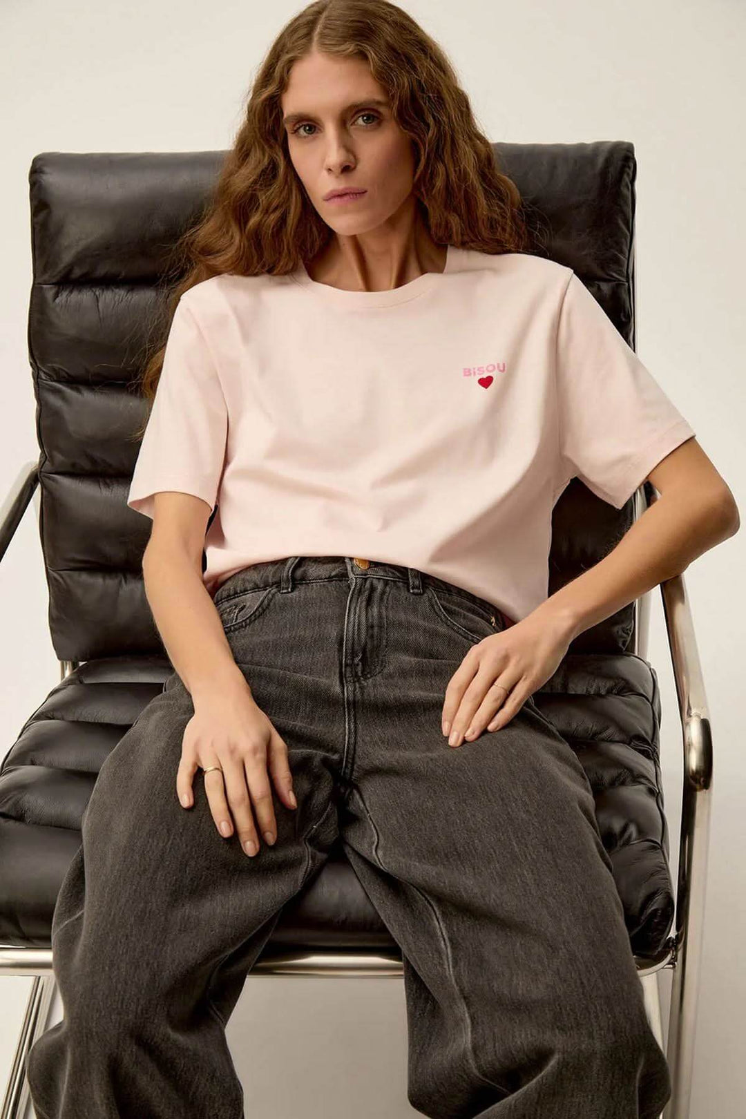 Femme portant un t-shirt rose doux Gazoline avec imprimé cœur, assise sur une chaise moderne.
