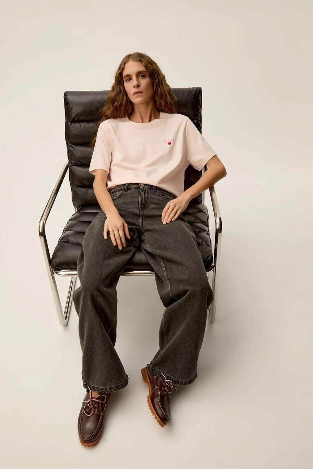 T-shirt Gazoline en rose nude avec imprimé "Bisous", porté par un modèle assis sur une chaise moderne.