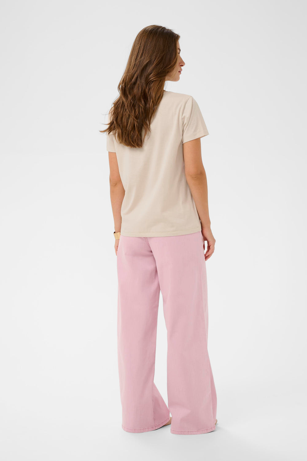 Vue arrière d'une femme portant un T-shirt Joliy à manches courtes avec un imprimé artistique, associé à un pantalon rose. Mode décontractée et féminine.