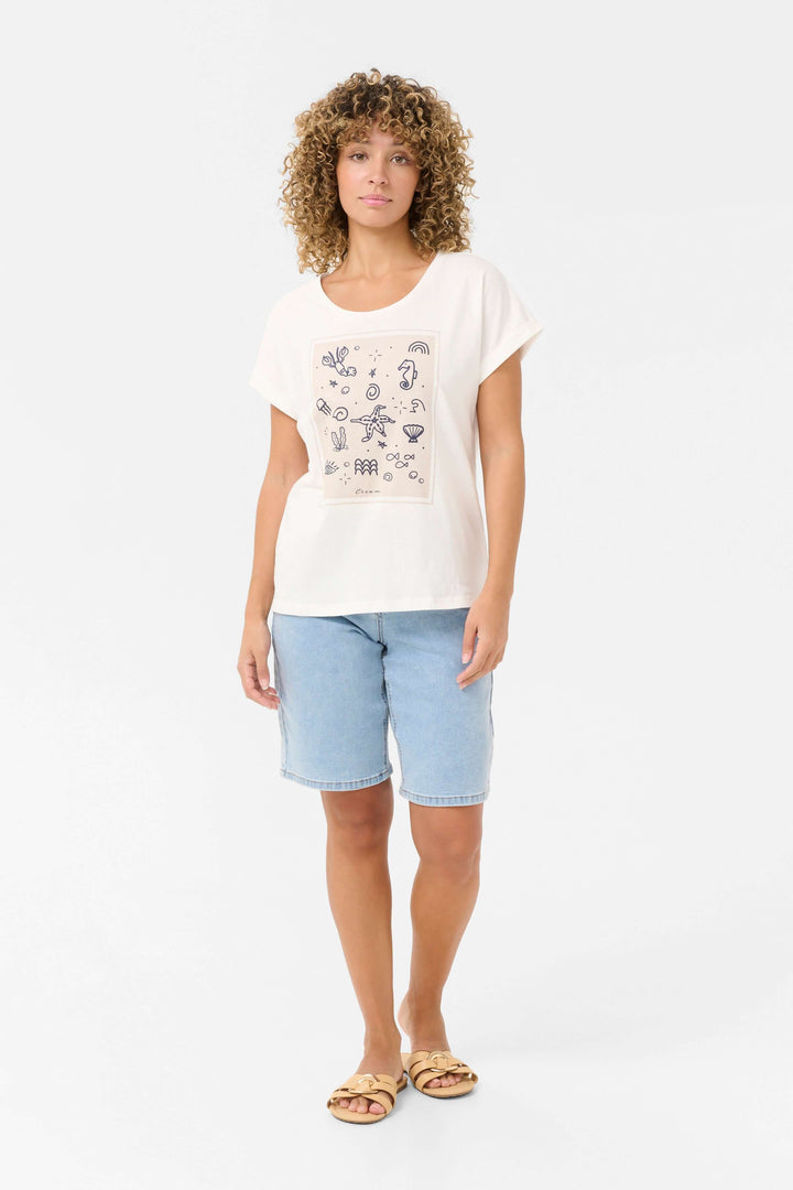 T-shirt Juka en coton avec imprimé marin, coupe décontractée et manches retournées, porté avec un short en jean.