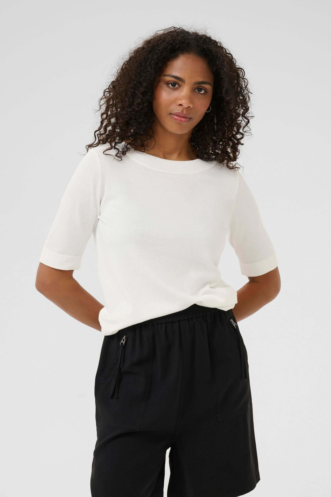 T-shirt Lizza en blanc avec manches mi-longues, porté avec un short noir, élégant et confortable.