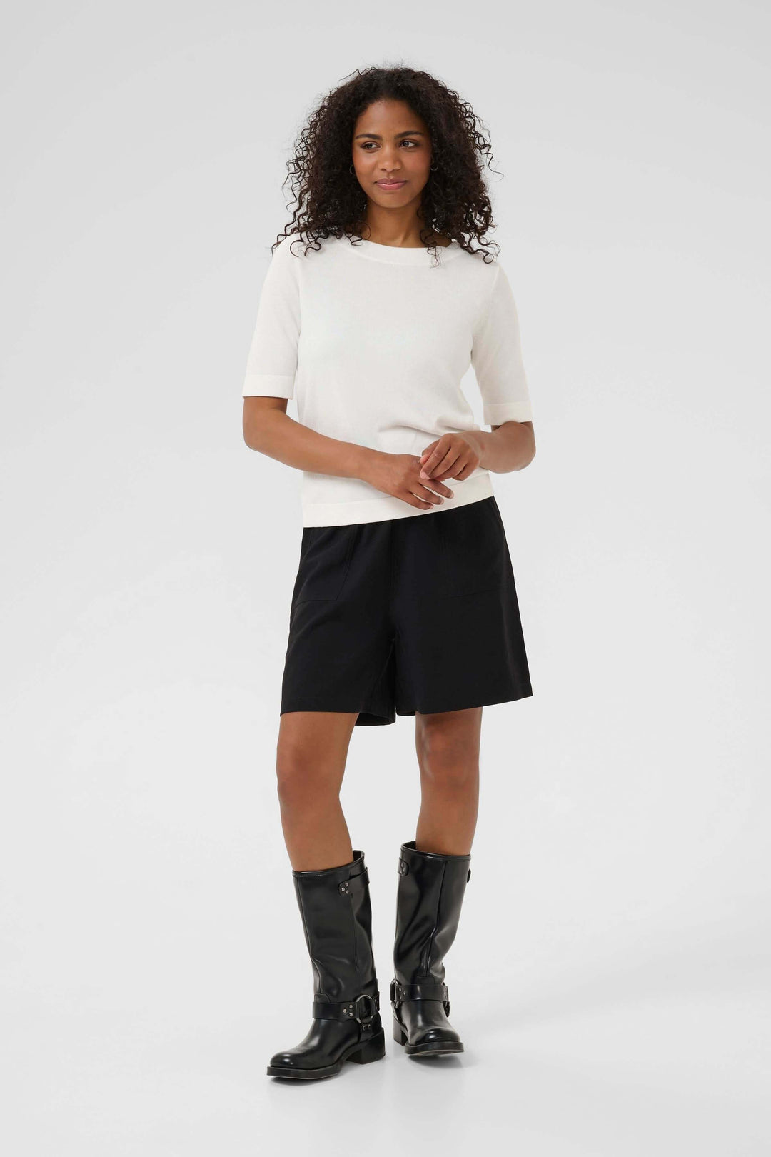 Modèle portant un T-shirt Lizza élégant en maille fine, associé à un short noir et des bottes noires.