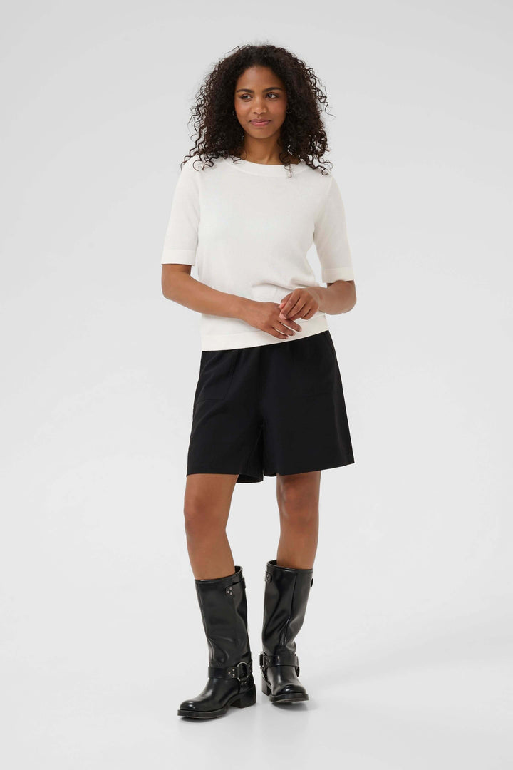 Modèle portant un T-shirt Lizza élégant en maille fine, associé à un short noir et des bottes noires.