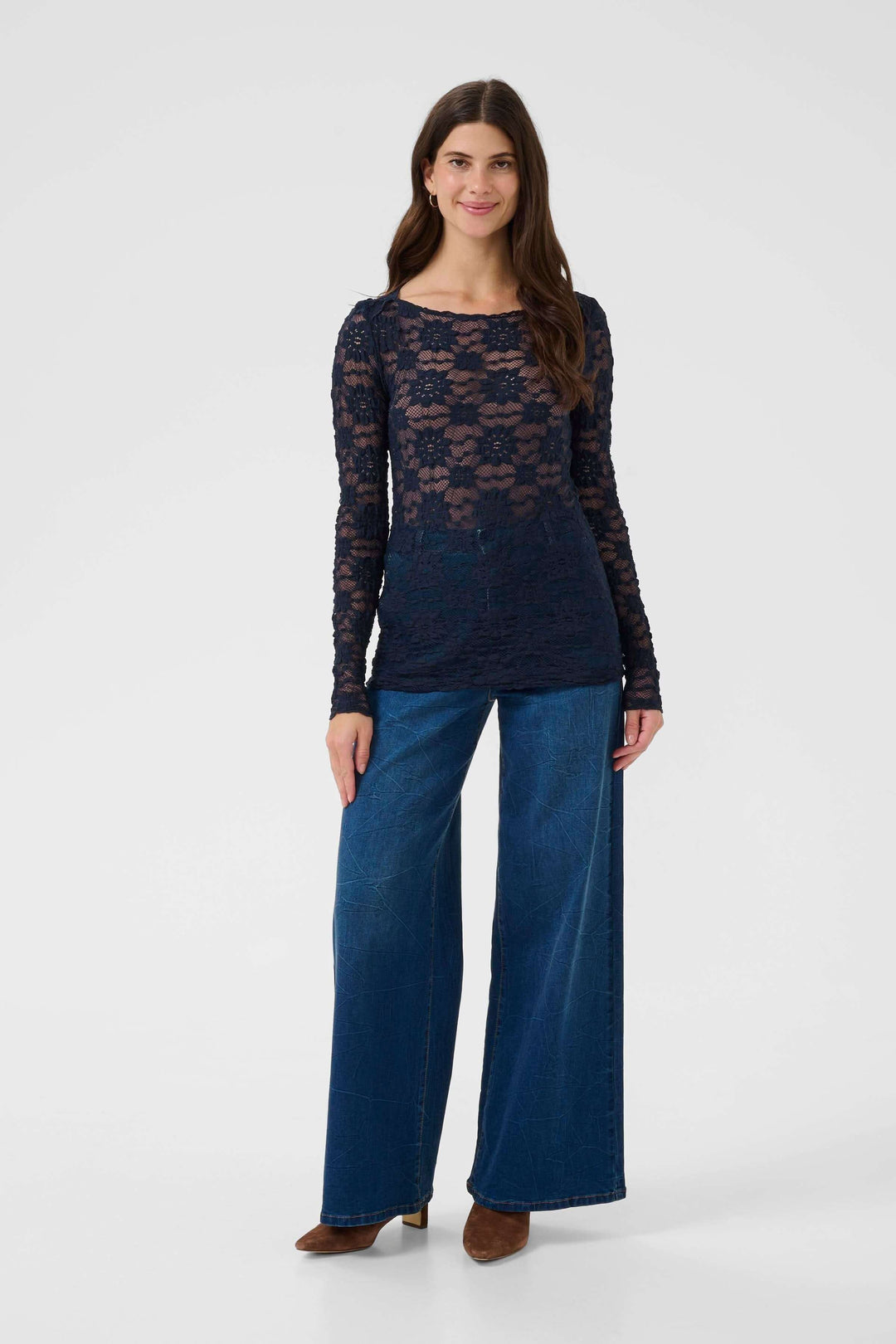 Femme portant le T-shirt Maddie en dentelle, manches longues, coupe ajustée, avec jean large, style raffiné et féminin.