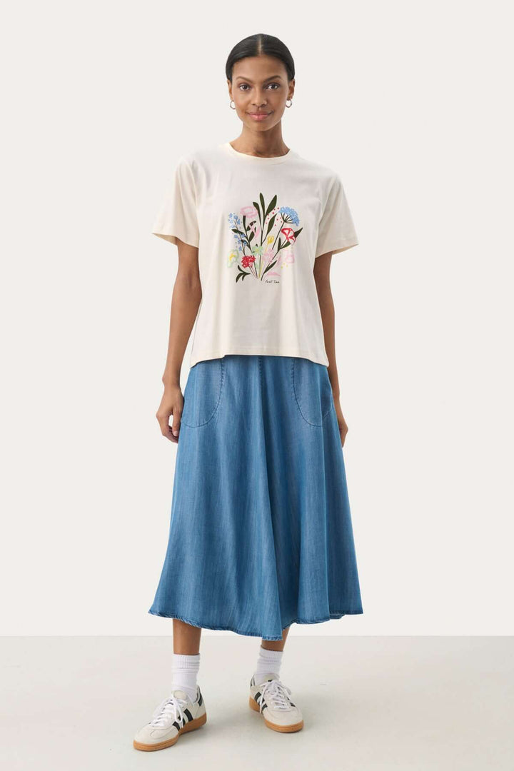 T-shirt en coton biologique avec imprimé floral, porté avec une jupe longue en denim, look casual et élégant.