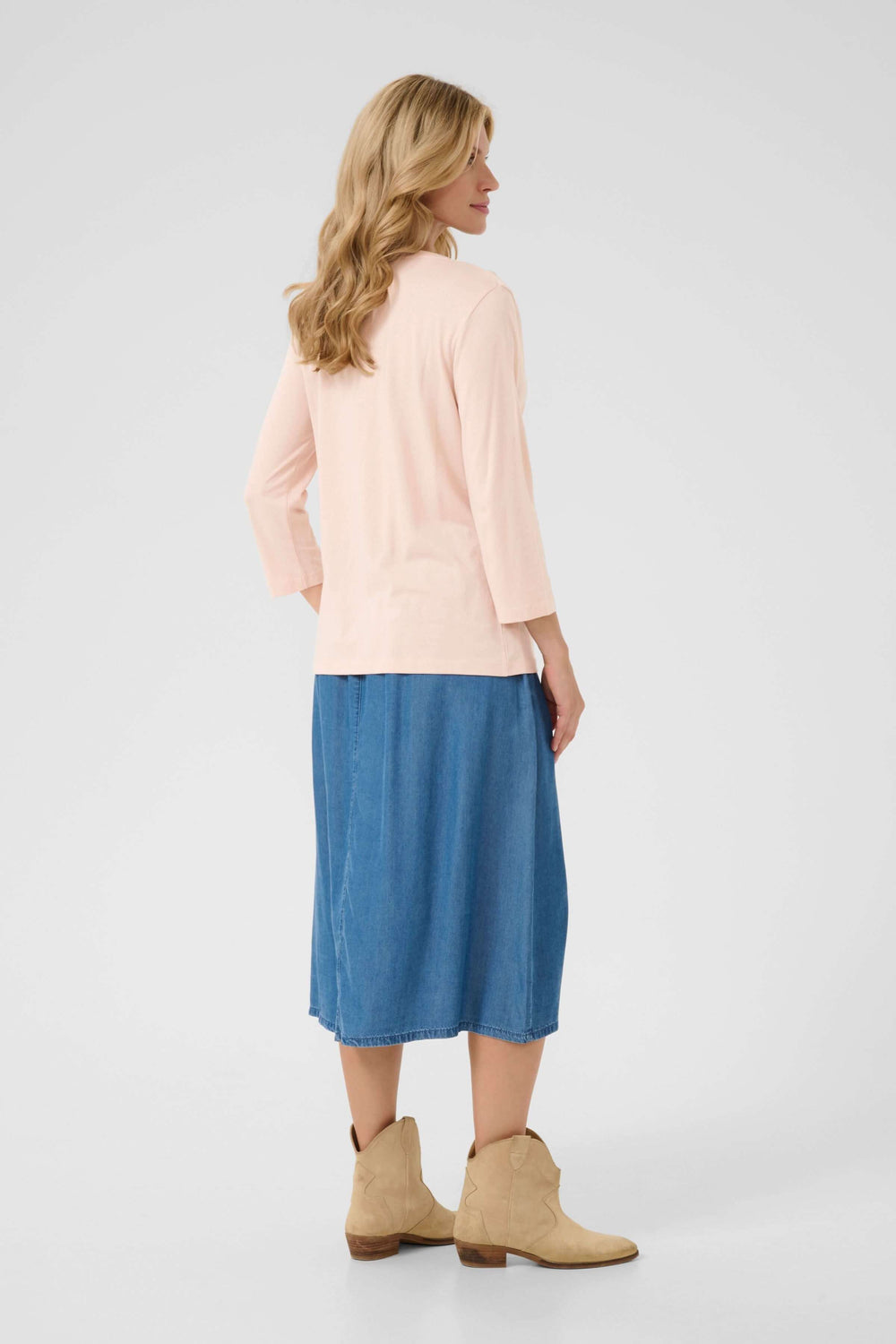 Femme vue de dos portant un t-shirt rose, une jupe en denim et des bottes beige, style décontracté.