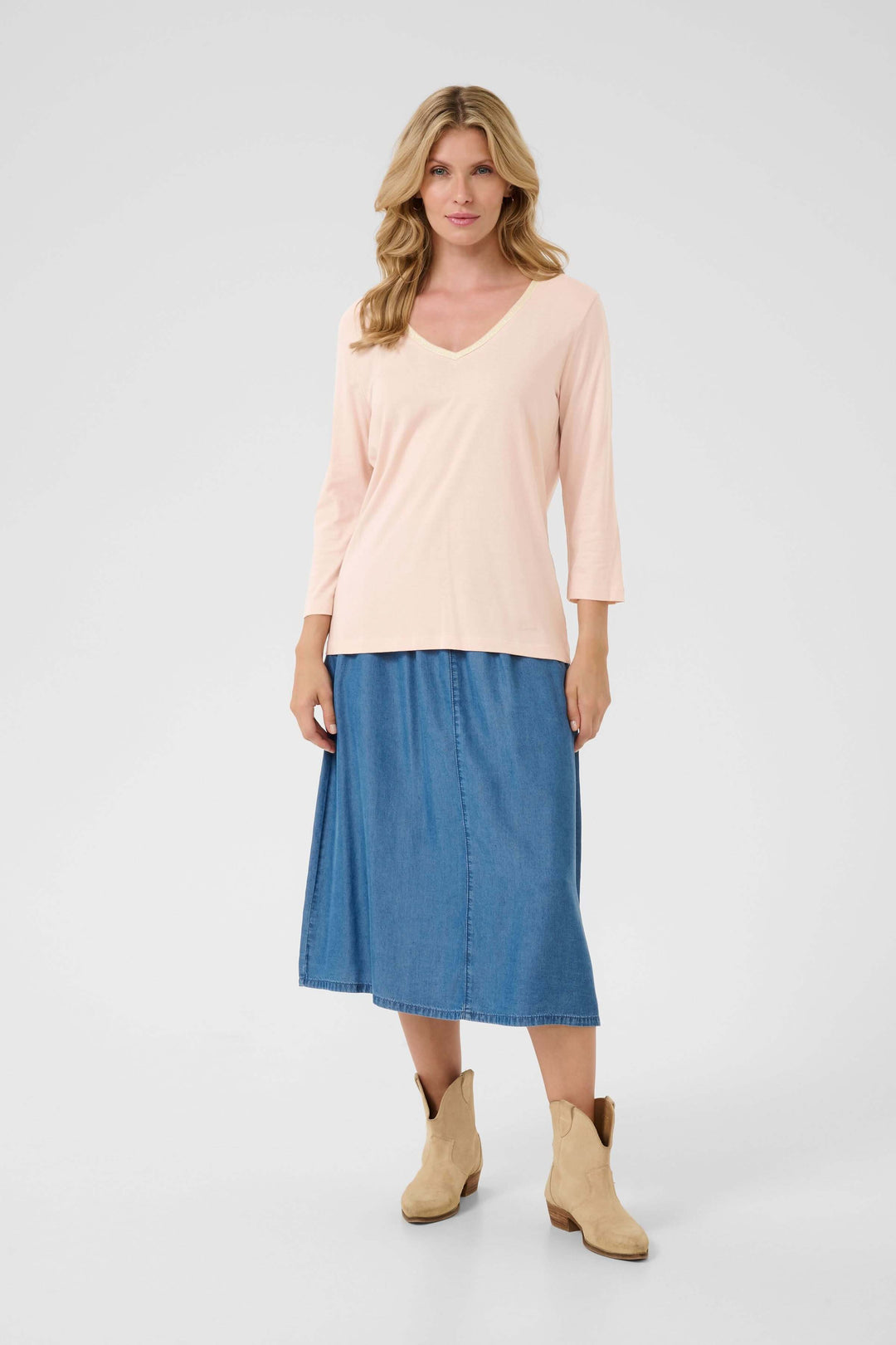 Femme portant un t-shirt Naia en coton doux avec encolure en V et manches trois-quarts, associé à une jupe en denim.