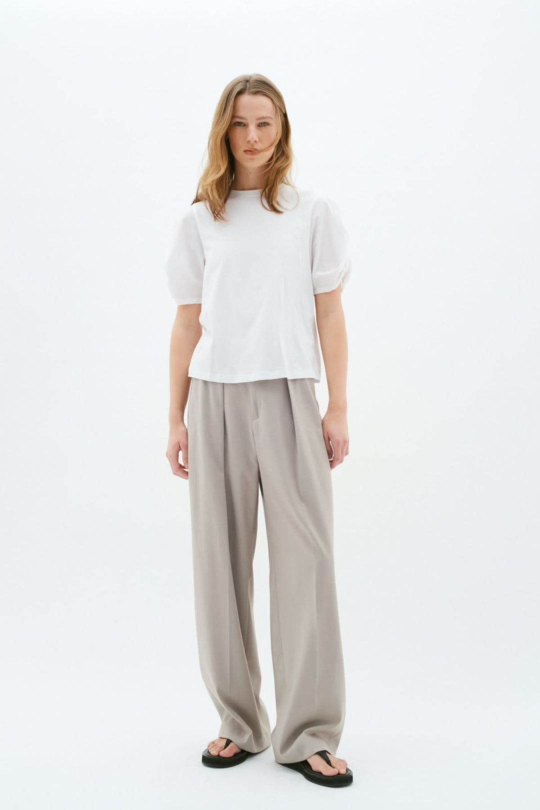 Femme portant un t-shirt blanc moderne avec manches froncées et pantalon ample gris.