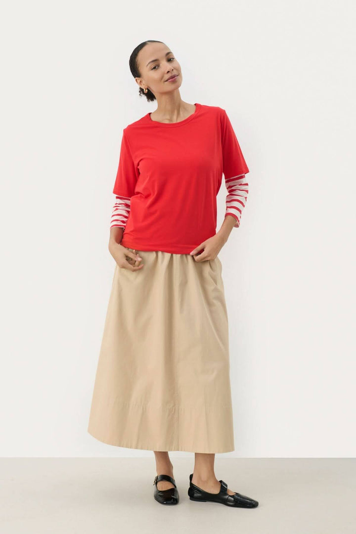 T-shirt Ratani rouge porté avec une jupe beige, offrant un look moderne et décontracté.