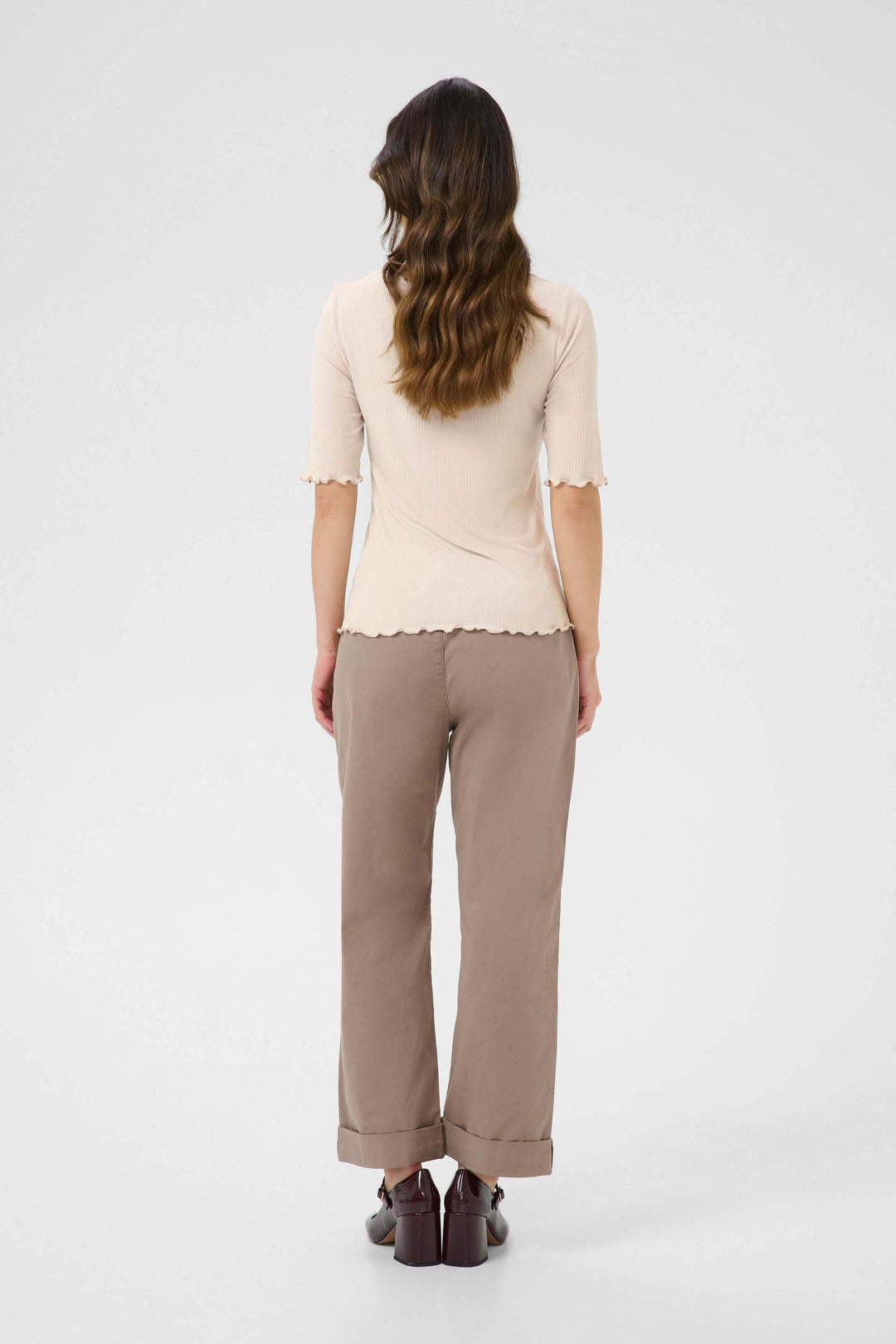 Femme vue de dos portant un T-shirt ajusté en jersey côtelé avec des bordures ondulées et un pantalon beige.