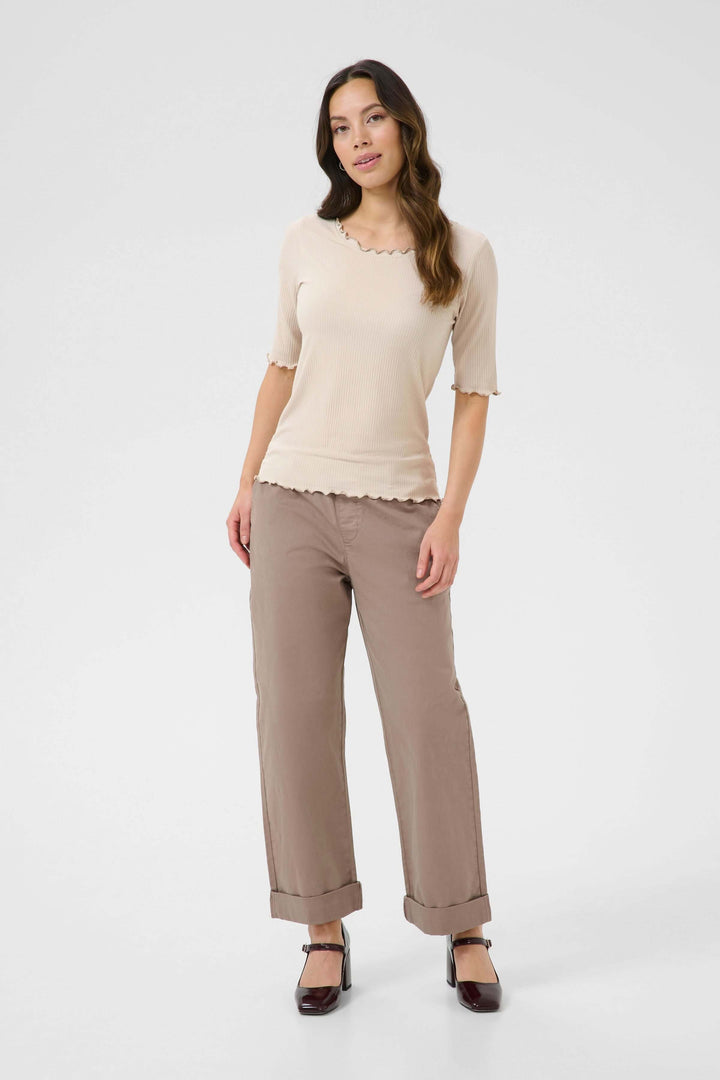 Femme portant un T-shirt ajusté en jersey côtelé beige avec bordures ondulées et pantalons beiges.
