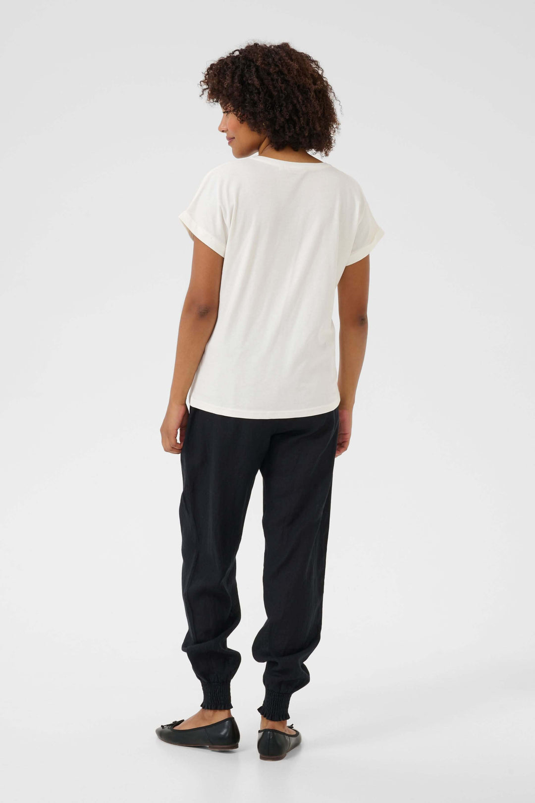 Femme portant un t-shirt en coton beige avec un style décontracté, vu de dos, associé à un pantalon noir.
