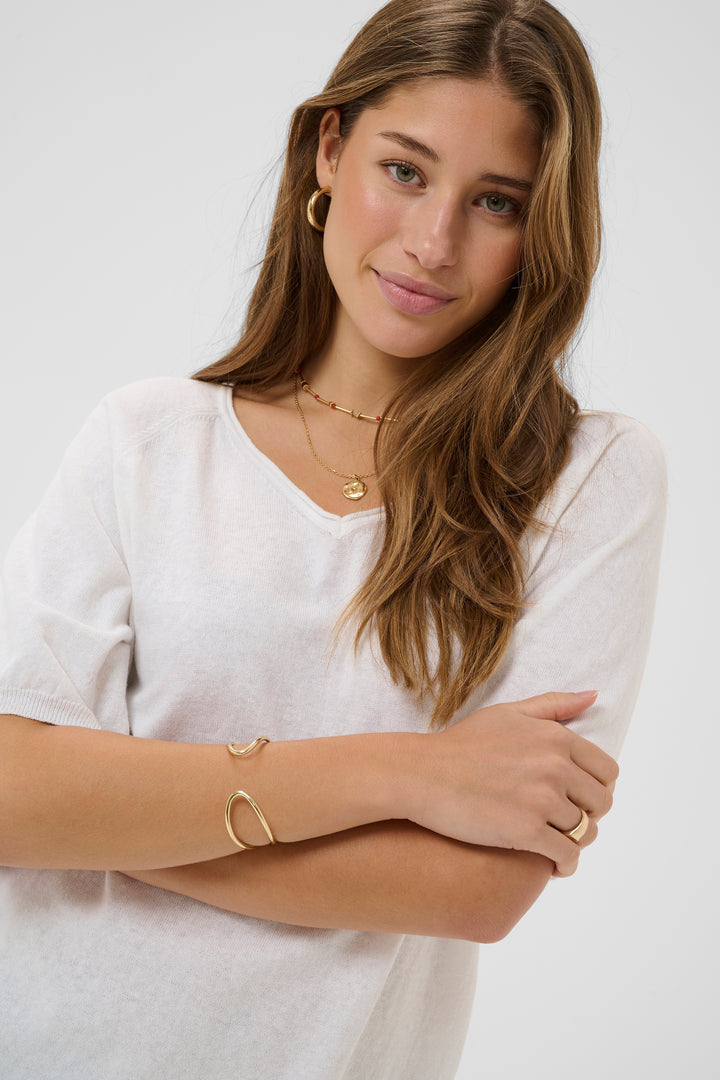 Femme portant un T-shirt Romane à encolure en V et manches amples, accessoirisé de bijoux dorés pour un look décontracté.