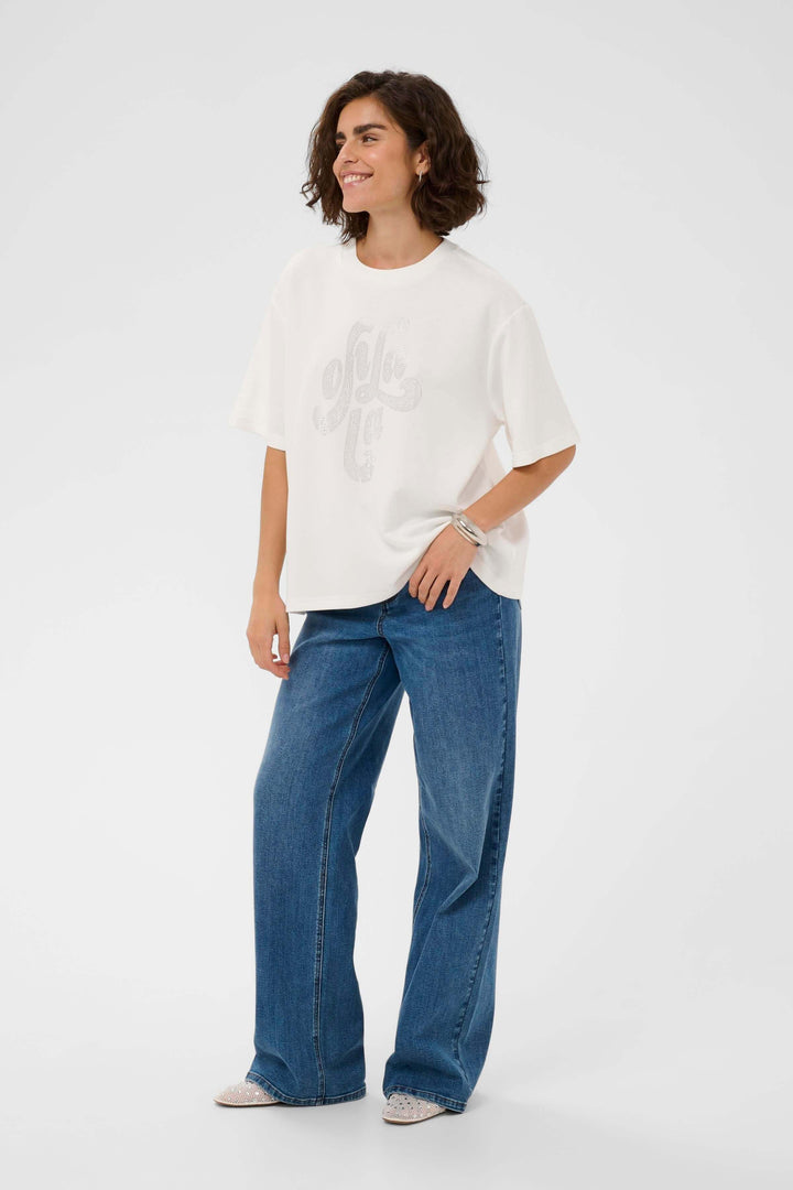 T-shirt Rosie en blanc porté par une femme, coupe ample et motif décoratif sur le devant, idéal pour un look moderne et décontracté.