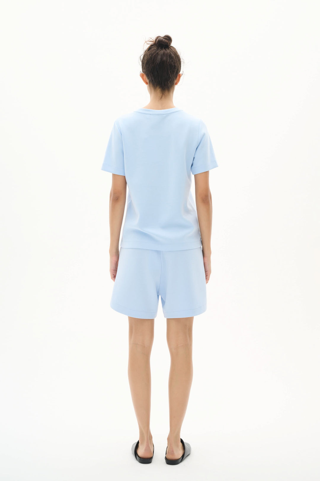 Model wearing a light blue T-shirt and matching shorts, showcasing a minimalist and modern outfit from the back.