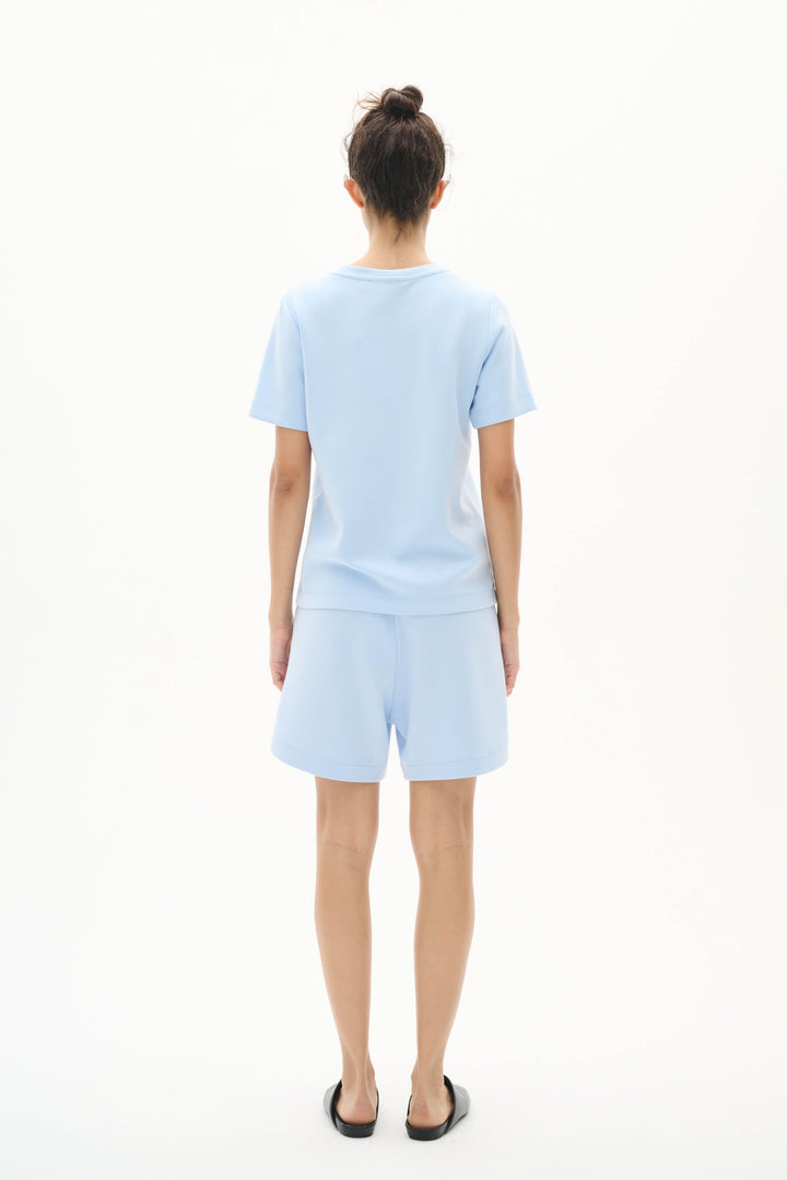 Model wearing a light blue T-shirt and matching shorts, showcasing a minimalist and modern outfit from the back.