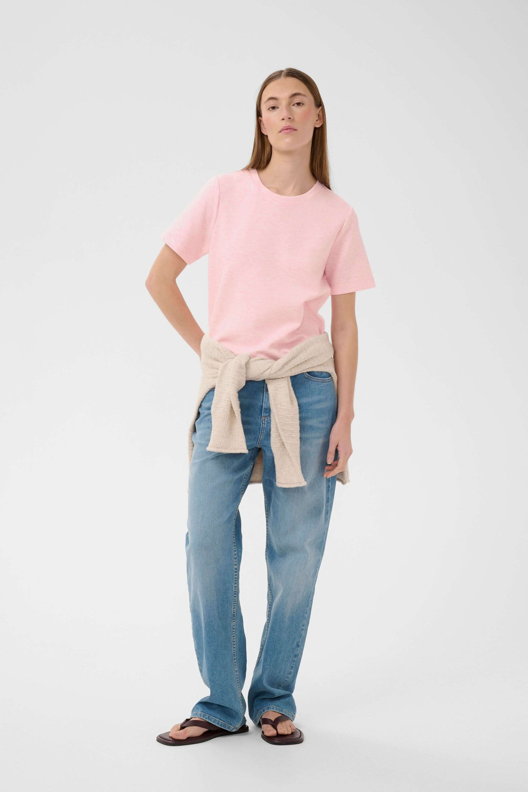 Femme portant le T-shirt Vincent rose, coupe droite, matière douce, associé à un jean et sandales noires, style décontracté.