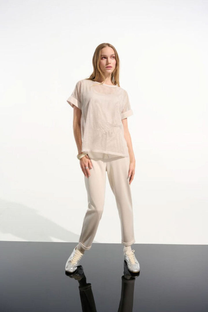 Femme portant un T-shirt ajouré fluide en maille légère avec manches courtes et ourlet droit, style moderne et décontracté.