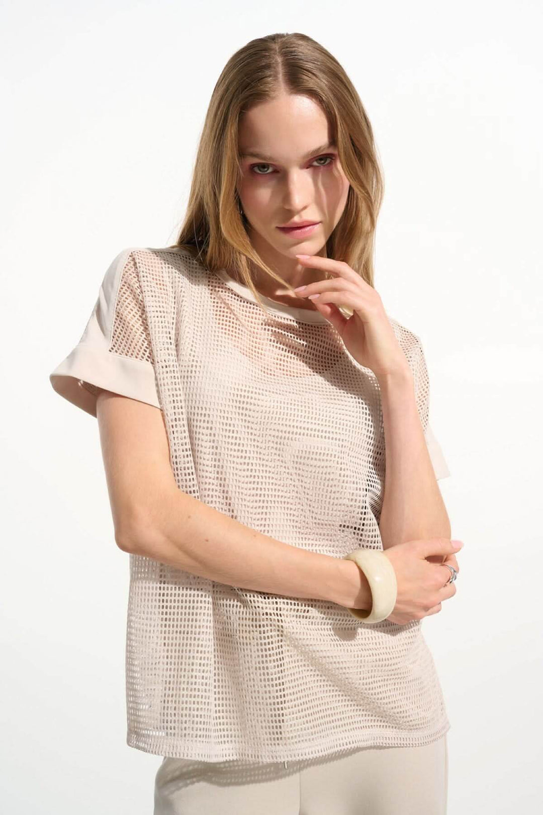 Femme portant un T-shirt ajouré fluide, style moderne avec manches courtes à revers, idéal pour un look contemporain et décontracté.