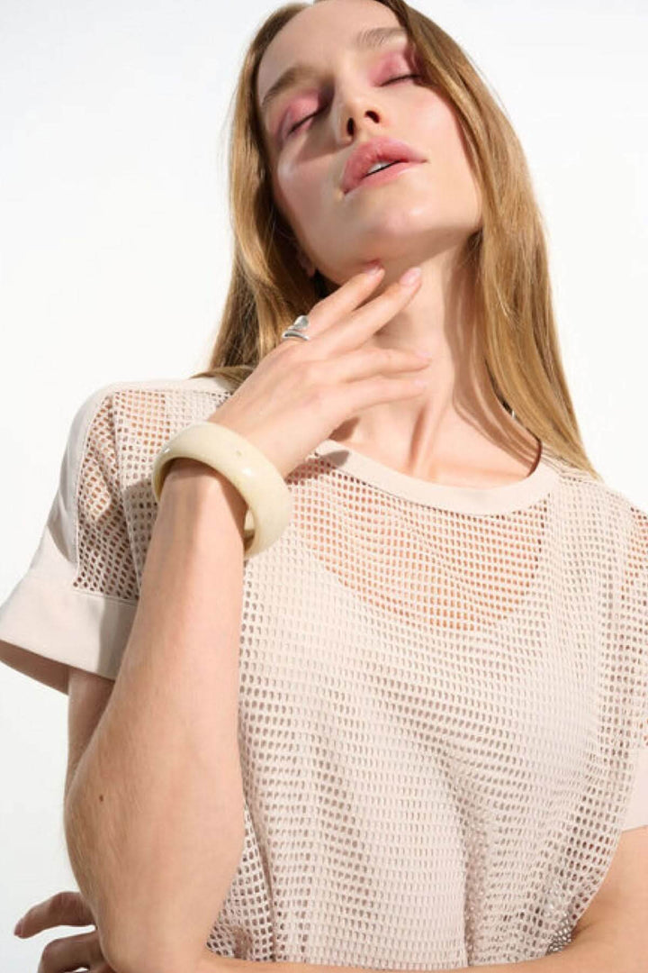 Femme portant un T-shirt ajouré fluide avec manches courtes et maille respirante, ajoutant une touche moderne à sa tenue.